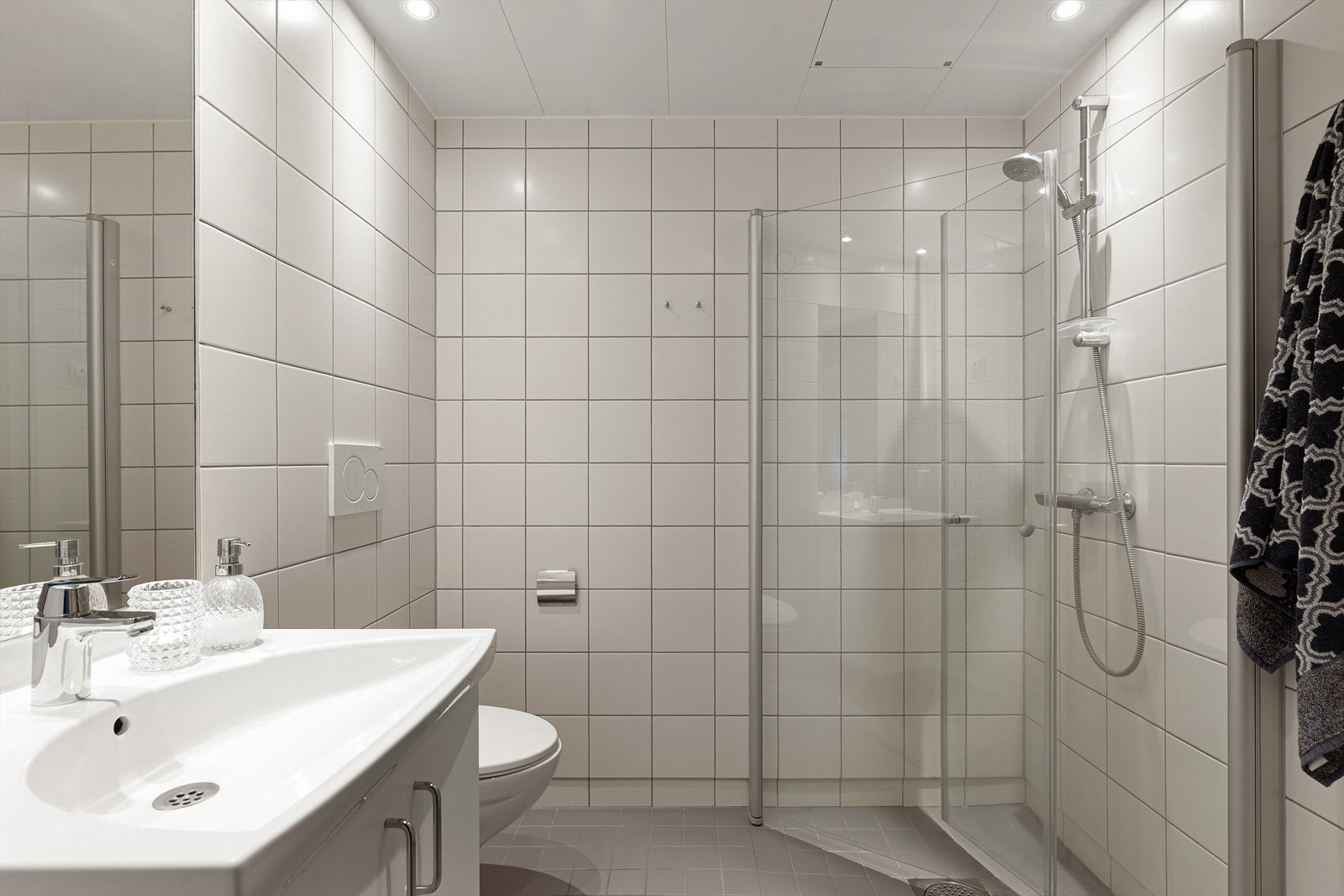 Rommet har åpen rørfordeling i himling over dusjsonen, varmekabler i gulv og folierte stålplater i himling med downlights. Galleribilde