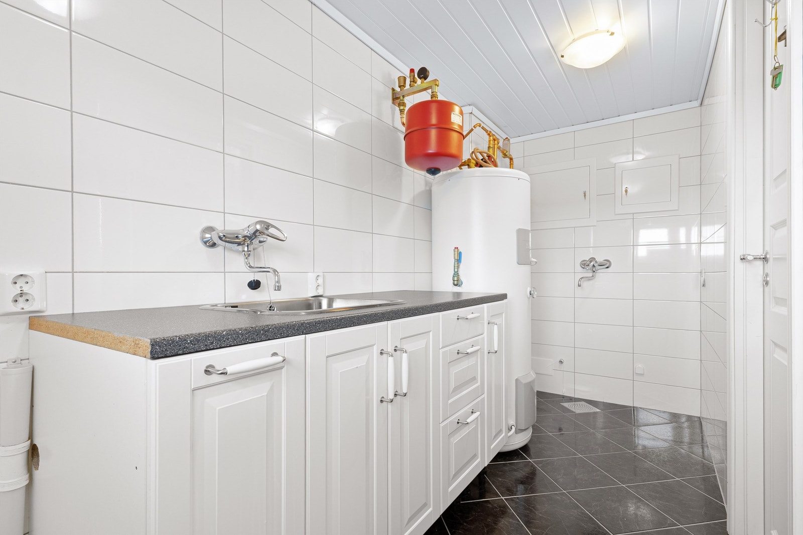 Praktisk vaskerom med utslagsvask i benkeskap, opplegg for vaskemaskin og skap for rør-i-rør system pusset opp i 2020. 200 L + 190 L dobbel mantlet bereder for forbruksvann og gulvvarme. Galleribilde