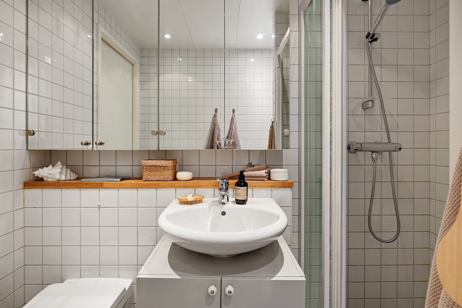 Badet er innredet med servant, underskap, speilskap, veggmontert toalett, dusjvegger/hjørne og opplegg for vaskemaskin. Galleribilde