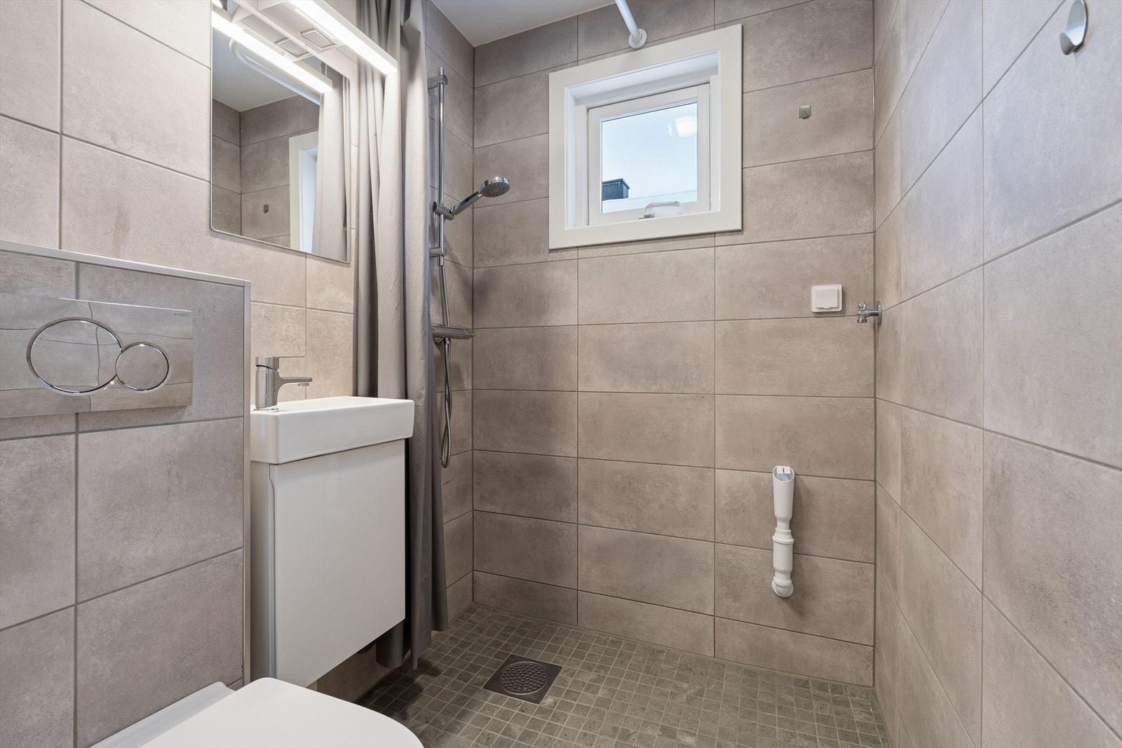 Baderommet ble pusset opp i 2024. Her er åpen dusj, servant med skap, vegghengt toalett og opplegg til vaskemaskin. Galleribilde