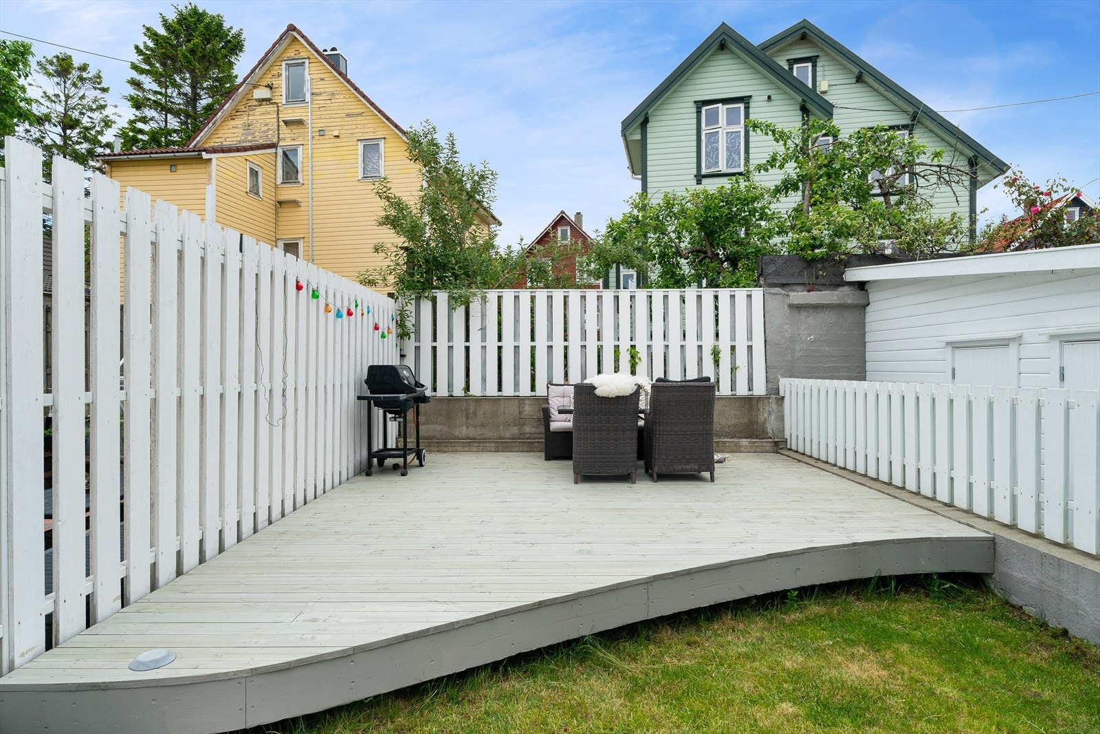 Sjarmerende uteområde med hvitmalte gjerder og felles terrasse. Perfekt for grilling og avslapning. Nærhet til rolig nabolag med idylliske hus. Galleribilde