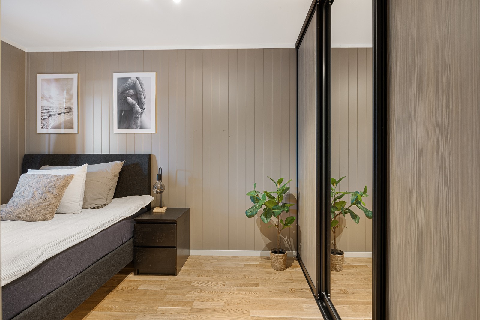 Det er mye oppbevaring i en plassbygd skyvedørsgarderobe med speilfronter i sort innramming. Galleribilde