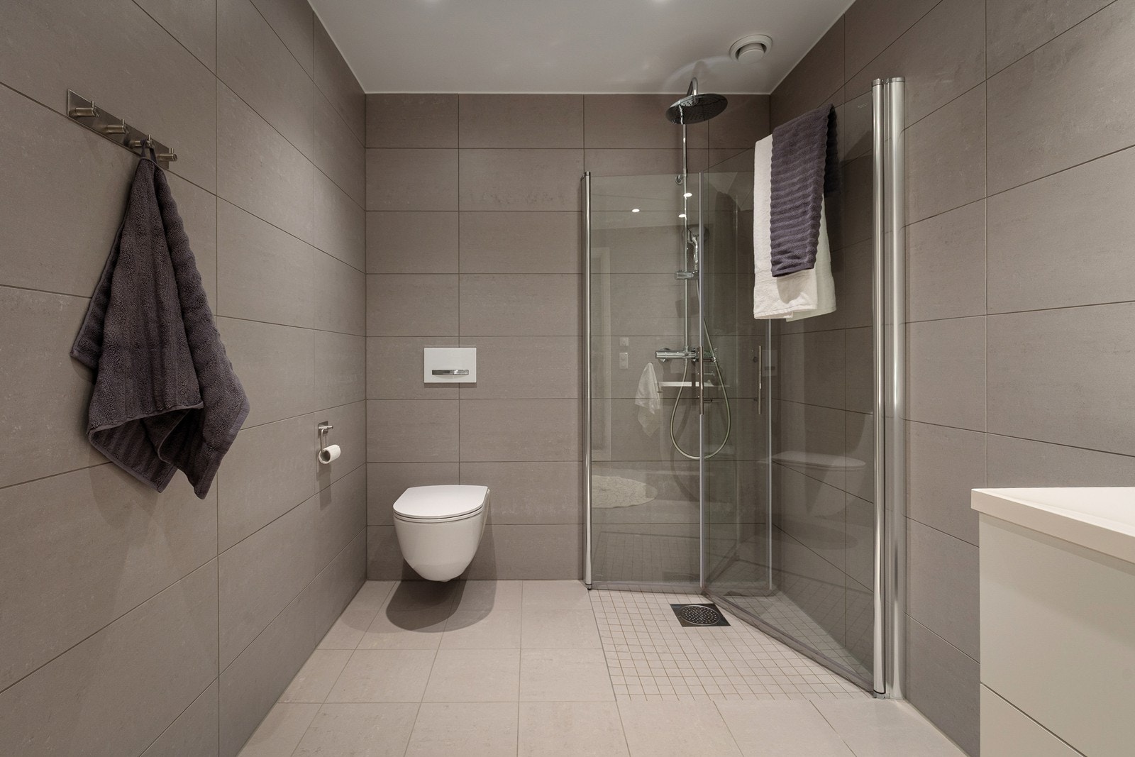 Hovedbadet har store, nøytrale fliser, vegghengt toalett og et romslig dusjhjørne. Galleribilde