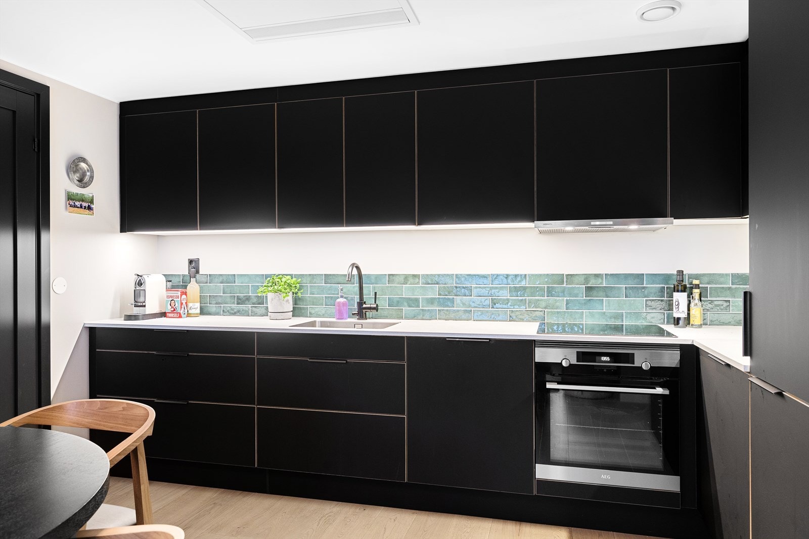 Kjøkkenet har glatte fronter i sort utførelse og laminat benkeplate med nedfelt vaskekum, samt overskap med belysning i underkant. Galleribilde