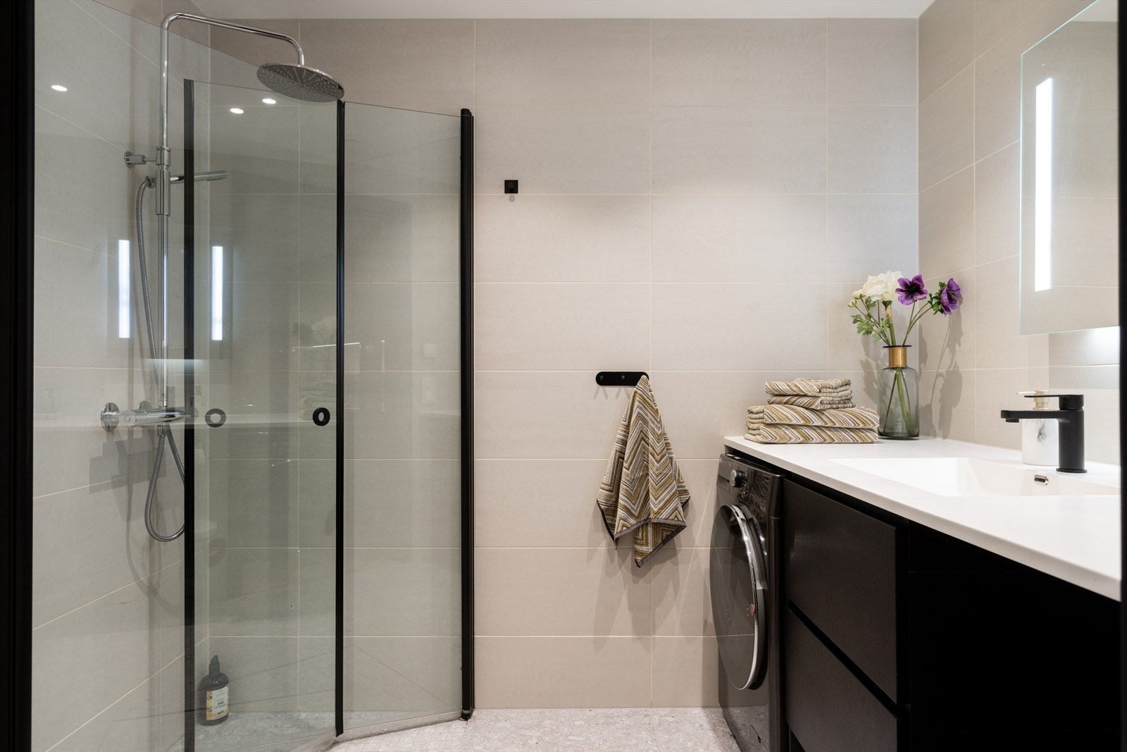 Delikat og moderne, flislagt baderom utført med store, beige fliser på vegger og gulv som gir et eksklusivt, rolig og helhetlig uttrykk. Badet har vannbåren gulvvarme og innfelte downlights i himlingen. Galleribilde