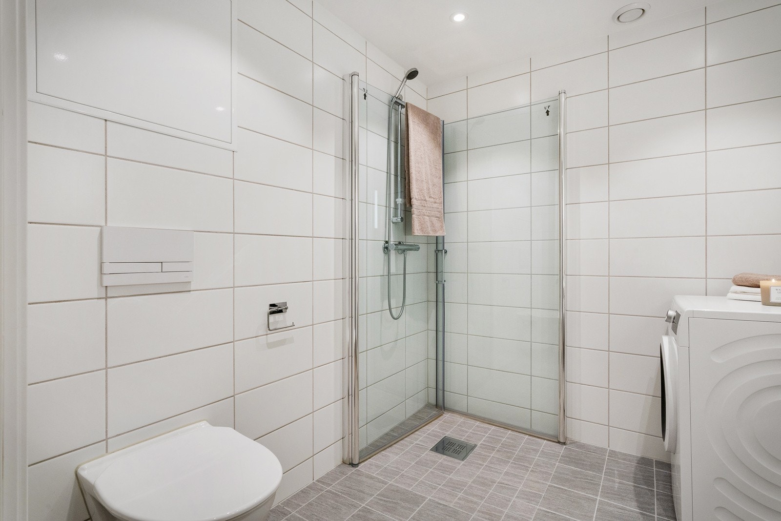 - Badet er lyst og klassisk utført med flislagte overflater, vegghengt toalett, servant med skuffer og dusjløsning med glassdører - Galleribilde