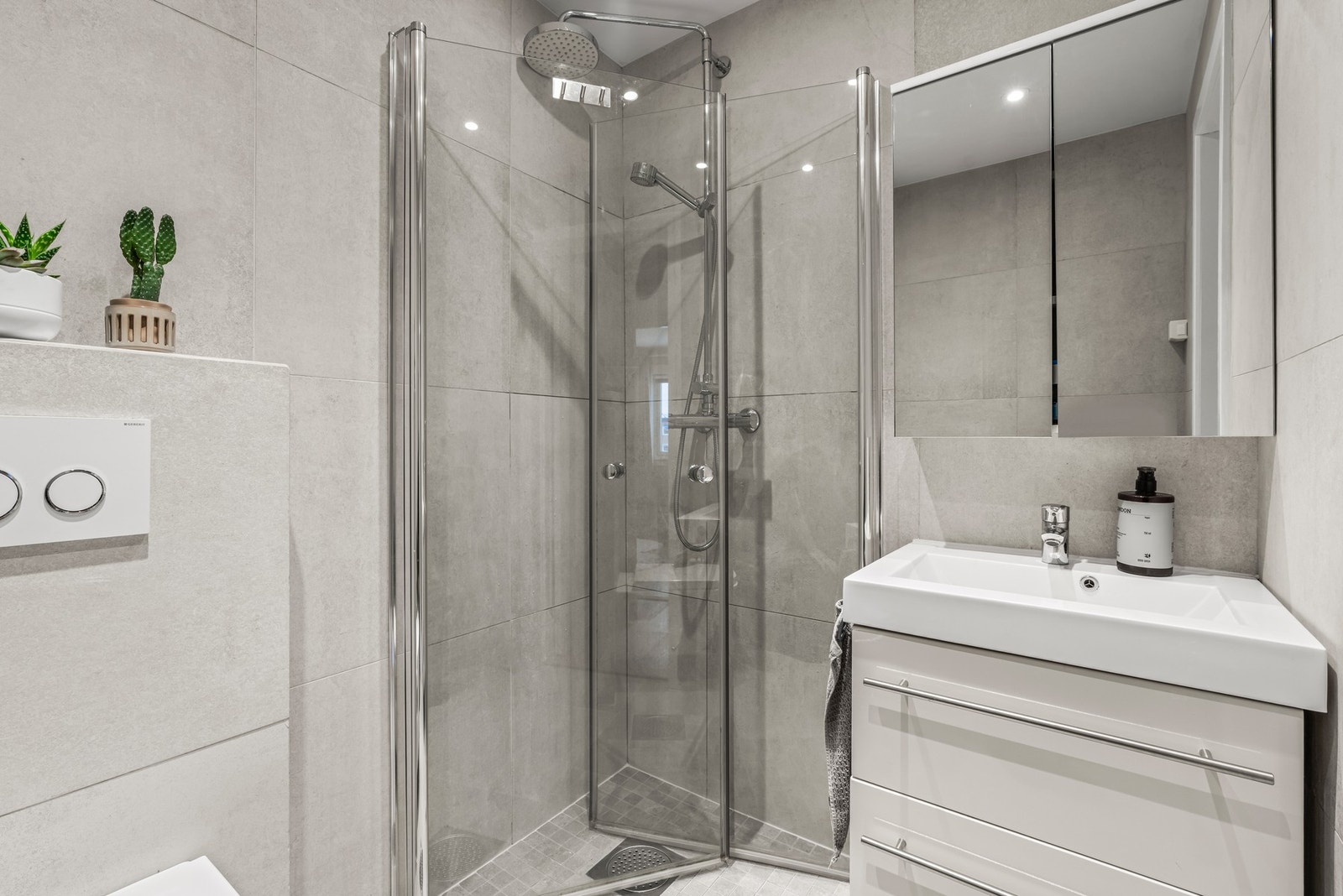 Videre er badet utstyrt med vegghengt toalett, dusjhjørne med to skyvbare glassdører og opplegg for vaskemaskin. Galleribilde