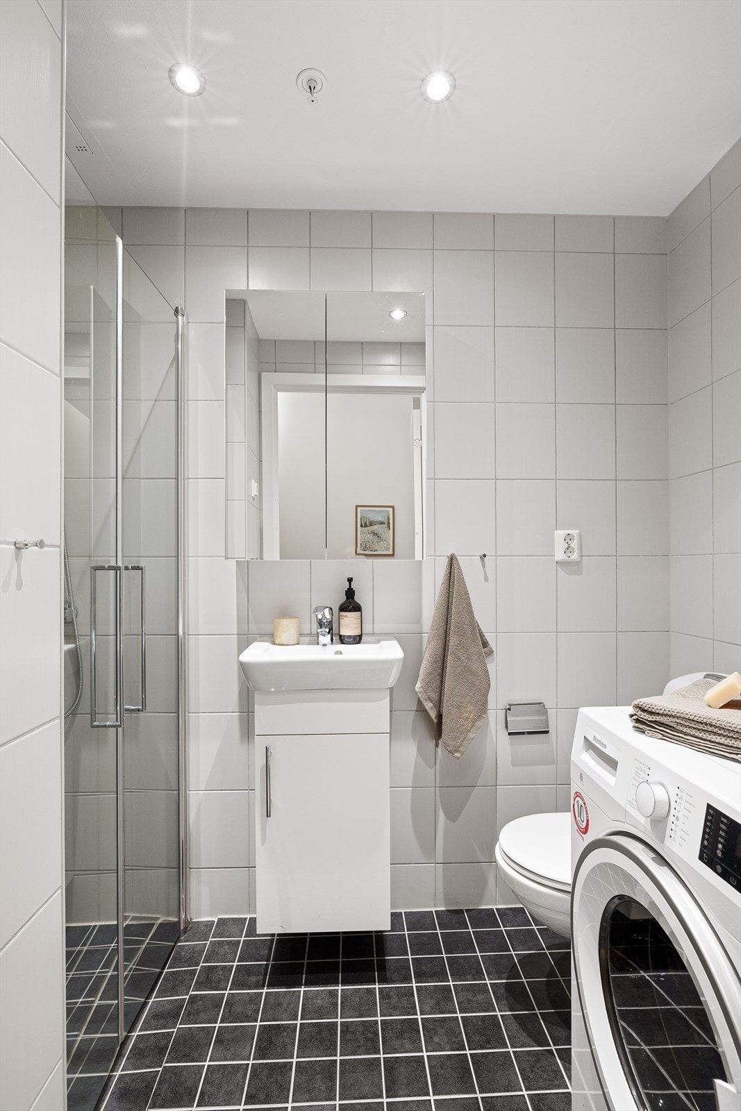 Hybel med dusj, vegghengt toalett, servant med skap under, speilskap og opplegg for vaskemaskin. Galleribilde