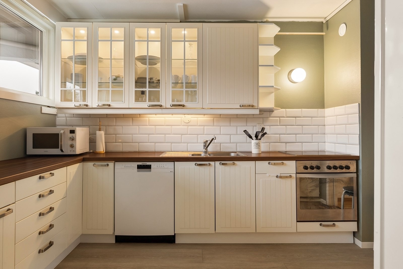 Lyst og trivelig kjøkken med belyst benk og profilerte fronter. Galleribilde