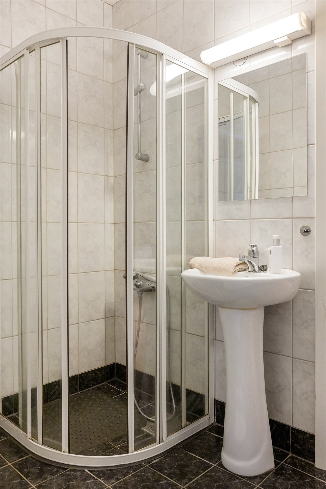 Flislagt baderom med dusjkabinett, servant og speil med belysning. Galleribilde