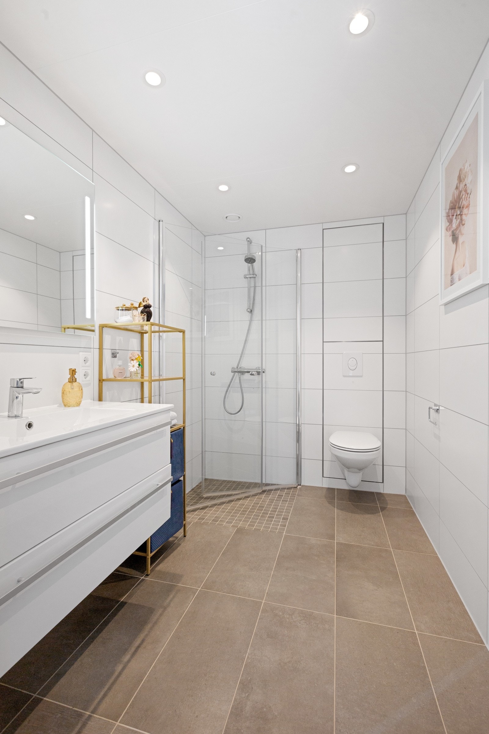 Badet med direkte adkomst til soverommet har vegghengt toalett, dusjhjørne med innfellbare dusjvegger samt vask med underskap og speil med innfelt lys Galleribilde