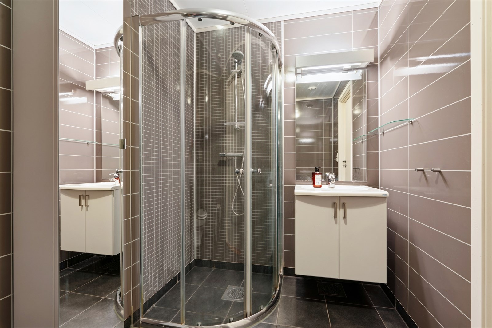 Rommet er innredet med speil, seksjon med servant, dusj og toalett. Galleribilde