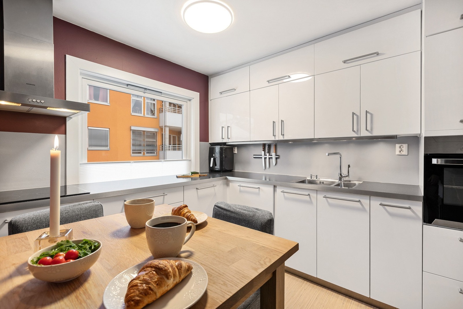 Moderne kjøkken med hvite, slette fronter. Integrerte hvitevarer, og stort vindu som gir mye naturlig lys. Galleribilde