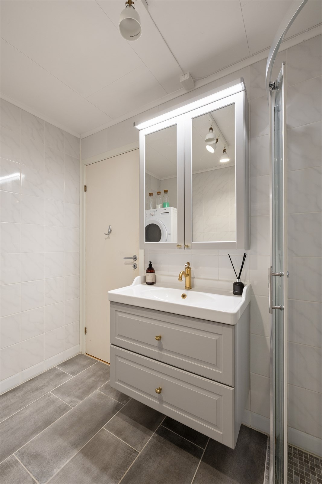 Rommet er innredet med en servant nedfelt i baderomsinnredning, dusjhjørne med dusjvegger og opplegg for vaskemaskin. Galleribilde