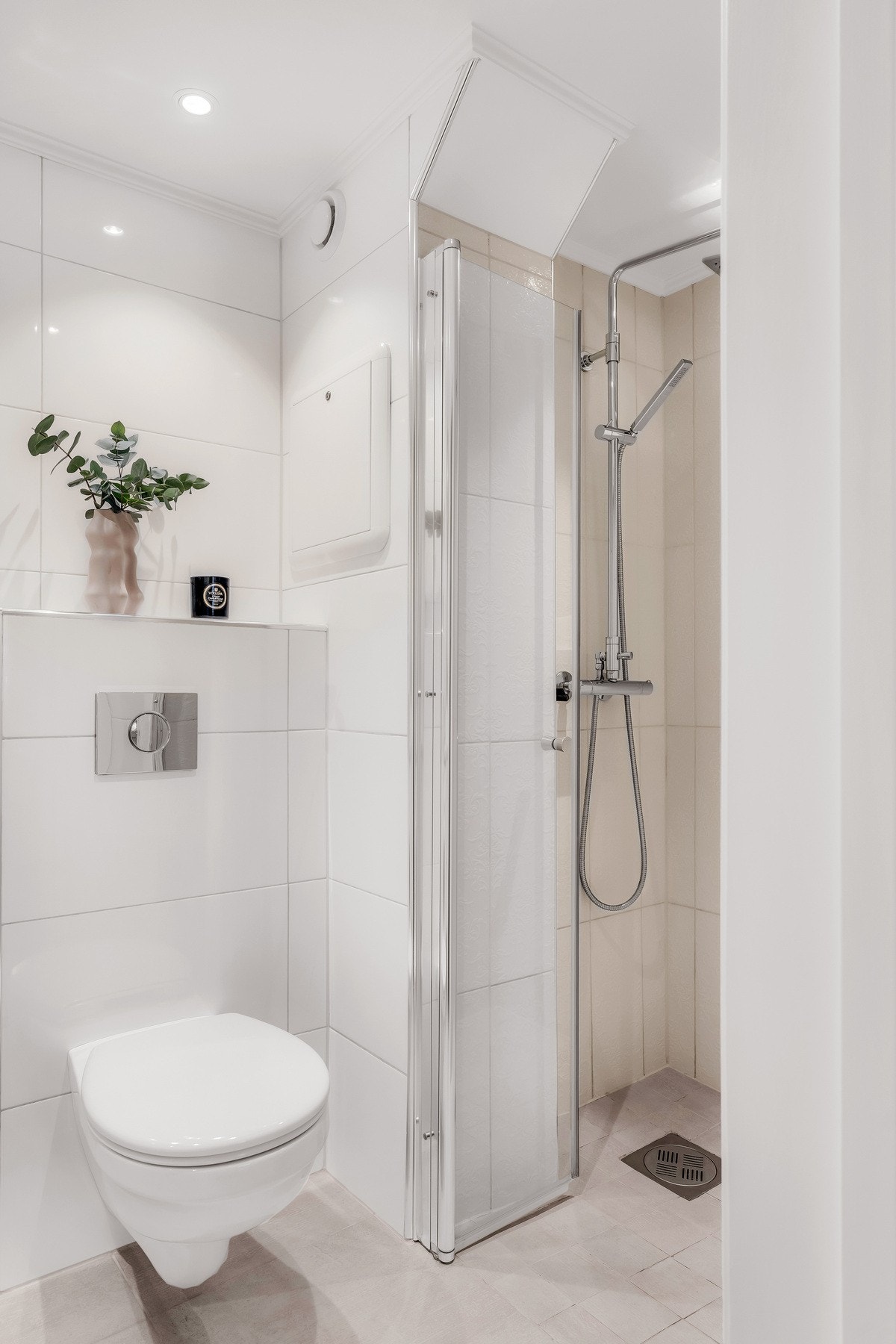 Videre er badet utstyrt med servant, skapinnredning, speil og flislagt dusjhørne. Toalettet er vegghengt og det er elektriske varmekabler i gulv. Galleribilde