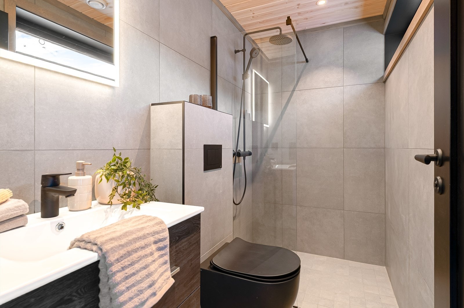 Helfliset bad ved gang med innredning med underskap, speil og belysning. Wc med innbygget sisterne og dusjhjørne med glassvegg Galleribilde