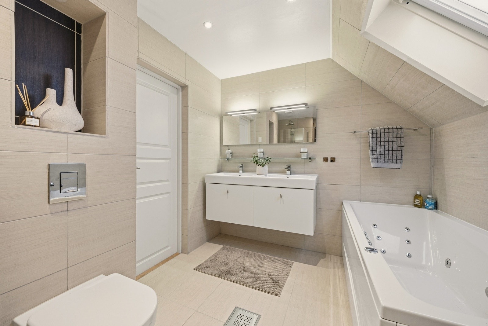 Badet inneholder: Vegghengt servantskap i slett utførelse. dobbelservant med ett-greps armatur. Speil med belysning over servant. badekar. Vegghengt toalett Galleribilde