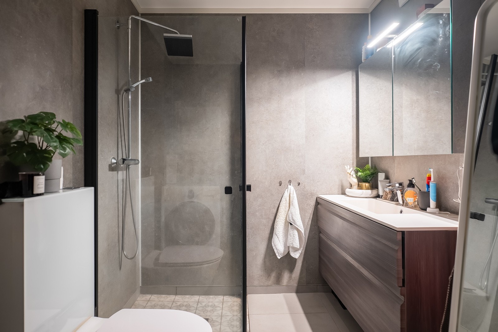 Flott, flislagt baderom med varmekabler i gulv. Bad kombineres med vaskerom, og er derfor innredet med opplegg for vaskemaskin i tillegg til dusjsone med vegger i glass, toalett, og servant med underskap. Galleribilde