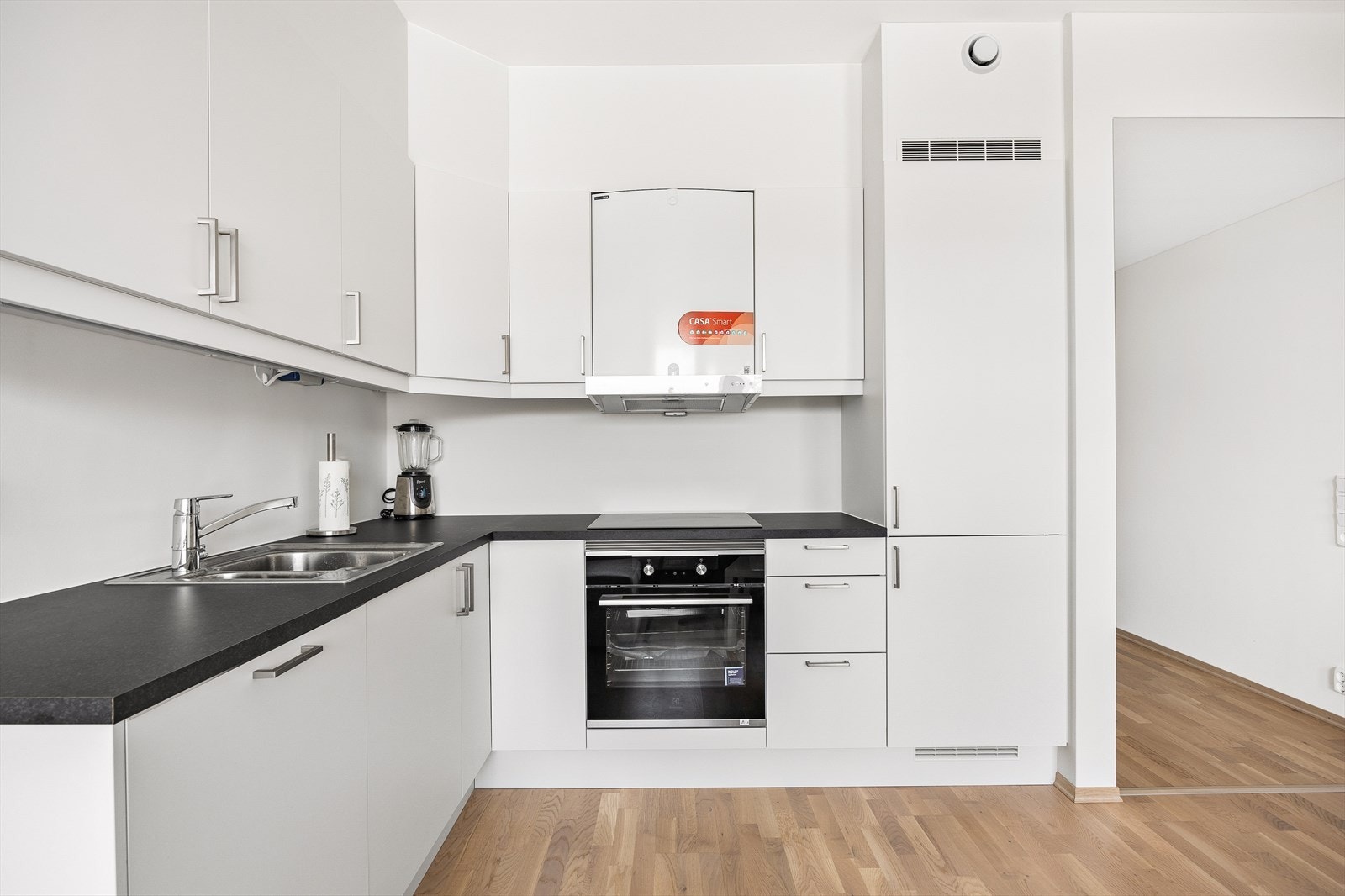 Kjøkkeninnredningen er hvit med slette fronter, laminat benkeplate og overskap som strekker seg til tak. Galleribilde