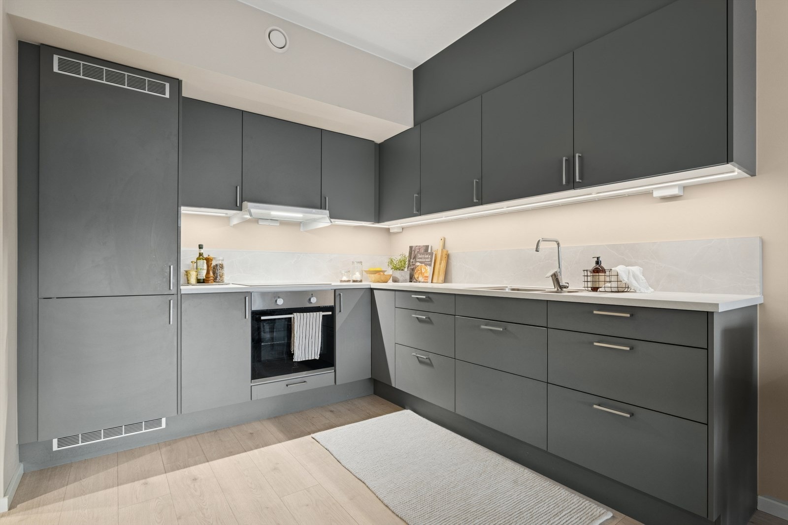 Kjøkkenet er i tidsriktige farger og fremstår moderne. Kjøkkenet er utstyrt med integrerte hvitevarer som kjøl/fryseskap, stekeovn, platetopp og ventilator. Det er klargjort for montering av oppvaskmaskin i skuffeseksjonen til høyre i bildet. Galleribilde