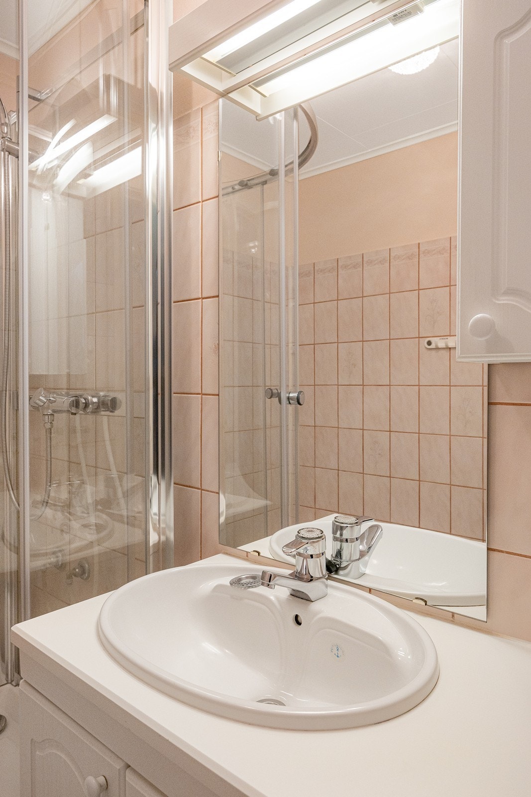 Innredningen har hvite skapfronter og benkeplate med nedfelt servant, matchende veggskap og speil. Galleribilde