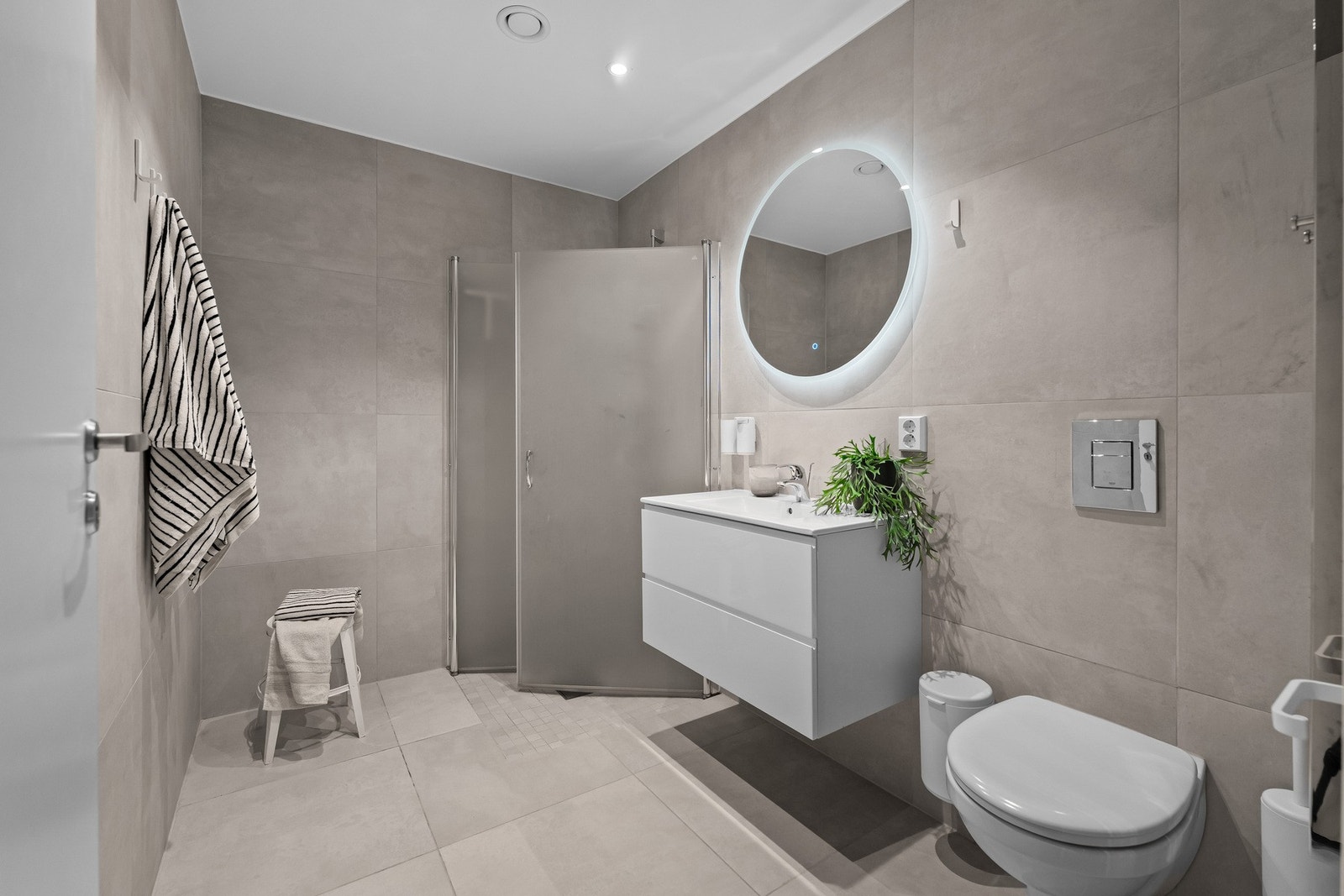 Bad nummer to ligger i boligens 2. etasje og holder en gjennomført god standard. Badet er innredet med servantmøbel med to skuffer i hvit utførelse, rundt speil, vegghengt toalett og separat dusjhjørne med innfellbare glassdører. Galleribilde