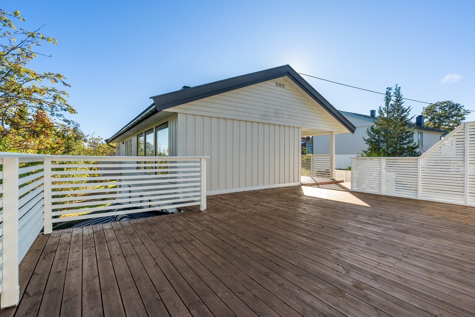 Terrassen ut fra stuen har noe overbygg slik at en også kan ha et par stoler under tak. Terrassen ble beiset i 2025 og rekkverket ble malt. Galleribilde