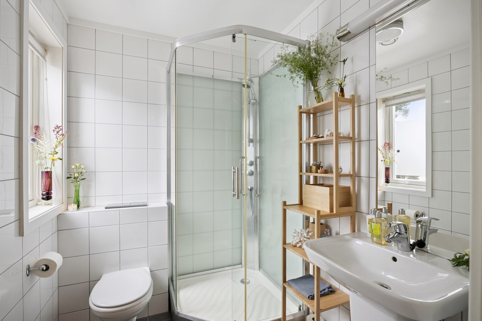 Pent flislagt bad utstyrt med dusjkabinett, vegghengt wc og lys servantinnredning. Det er varme i gulv. Galleribilde