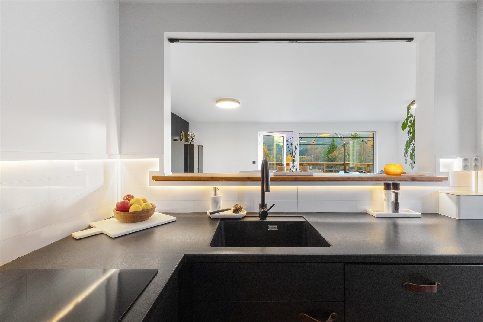 Fra kjøkkenet mot stuen og den romslige terrassen. LED belysning over kjøkkenbenk og pene fliser lagt i flukt med kjøkkenbenk. Galleribilde