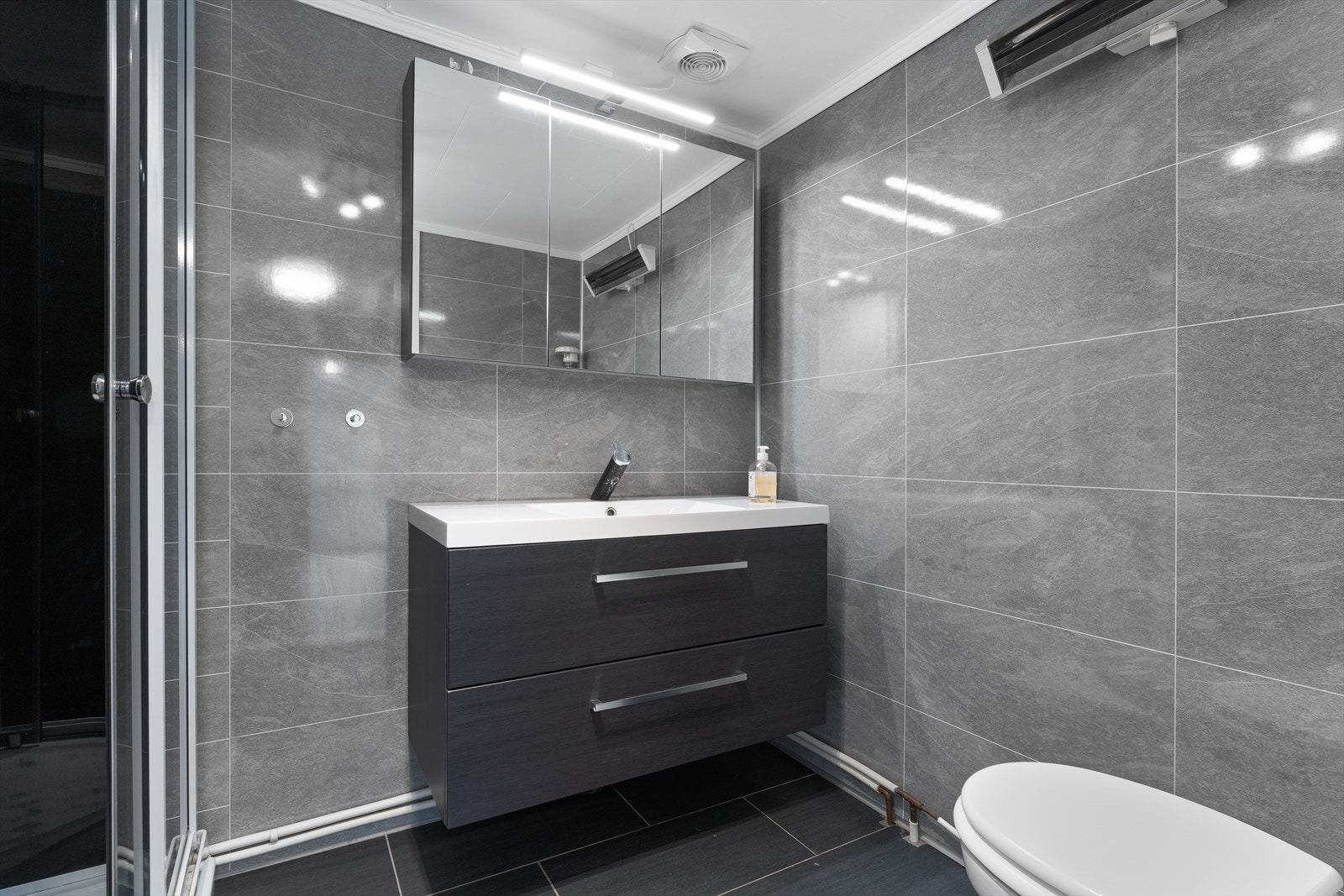 Moderne bad med stilrene grå fliser og elegant servantskap. Funksjonell belysning gir et lyst og innbydende preg. Galleribilde