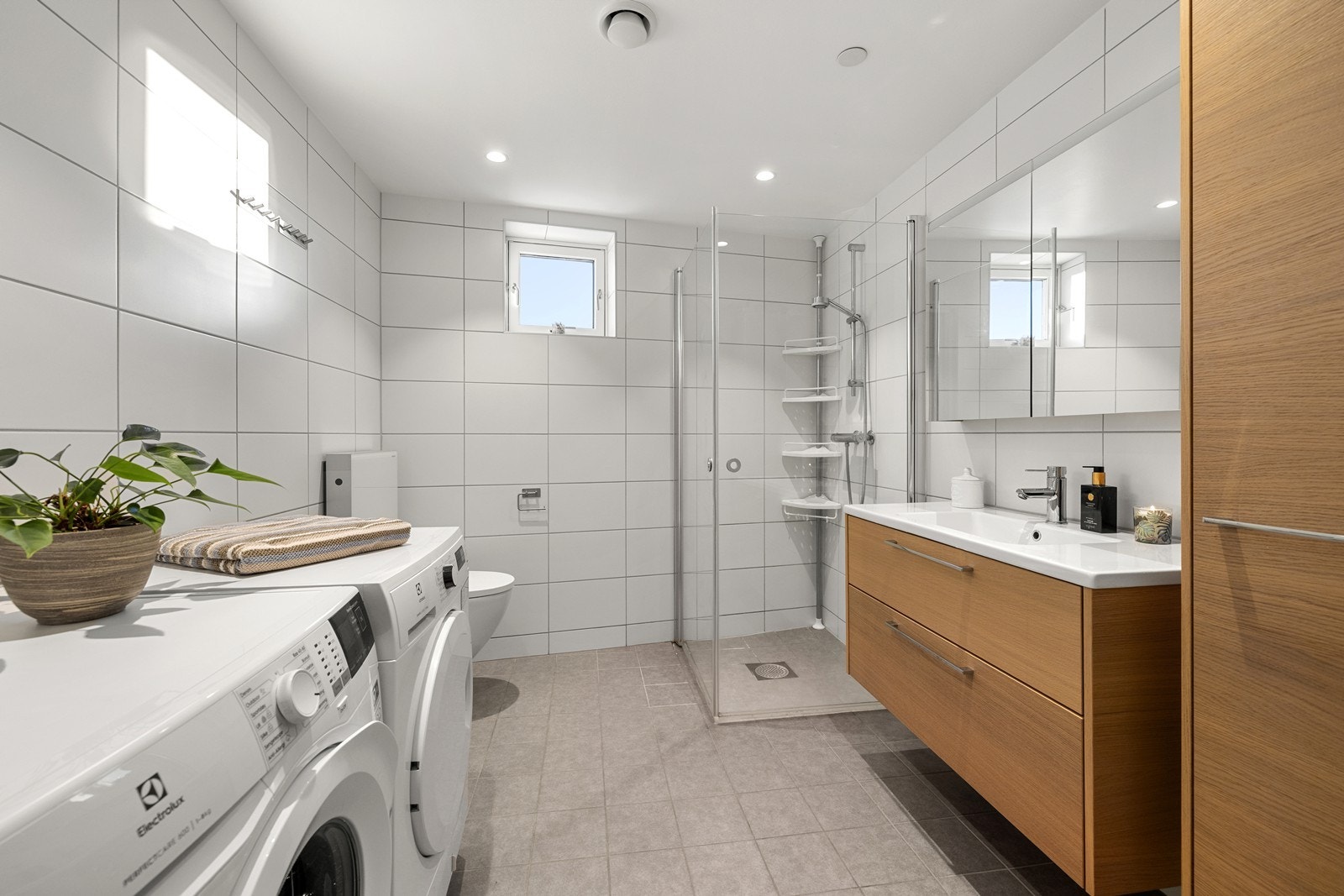 Romslig, flislagt bad med vegghengt toalett og dusjhjørne med glassdører. Galleribilde