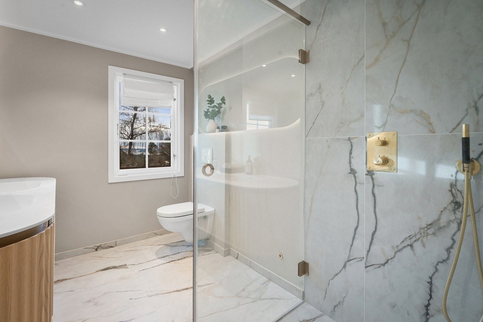 Baderom 2 (2 etasje - Rehabilitert 2025) - Flislagt baderom med dobbel servantseksjon og skuffer, dusjhjørne med skillevegg i herdet glass, veggheng toalett, og speil med integrert lys.