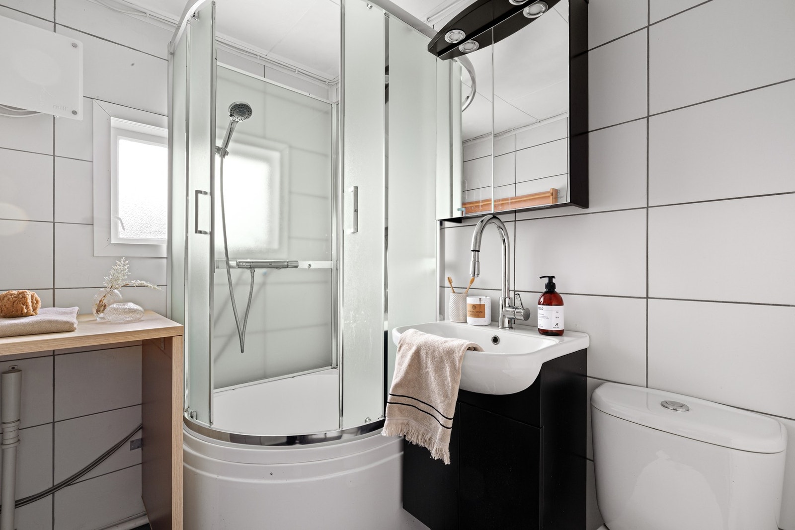 På badet er det toalett, panelovn og dusjkabinett. Den øvrige innredningen består av en arbeidsbenk, et sort servantskap og et matchende speilskap med belysning Galleribilde