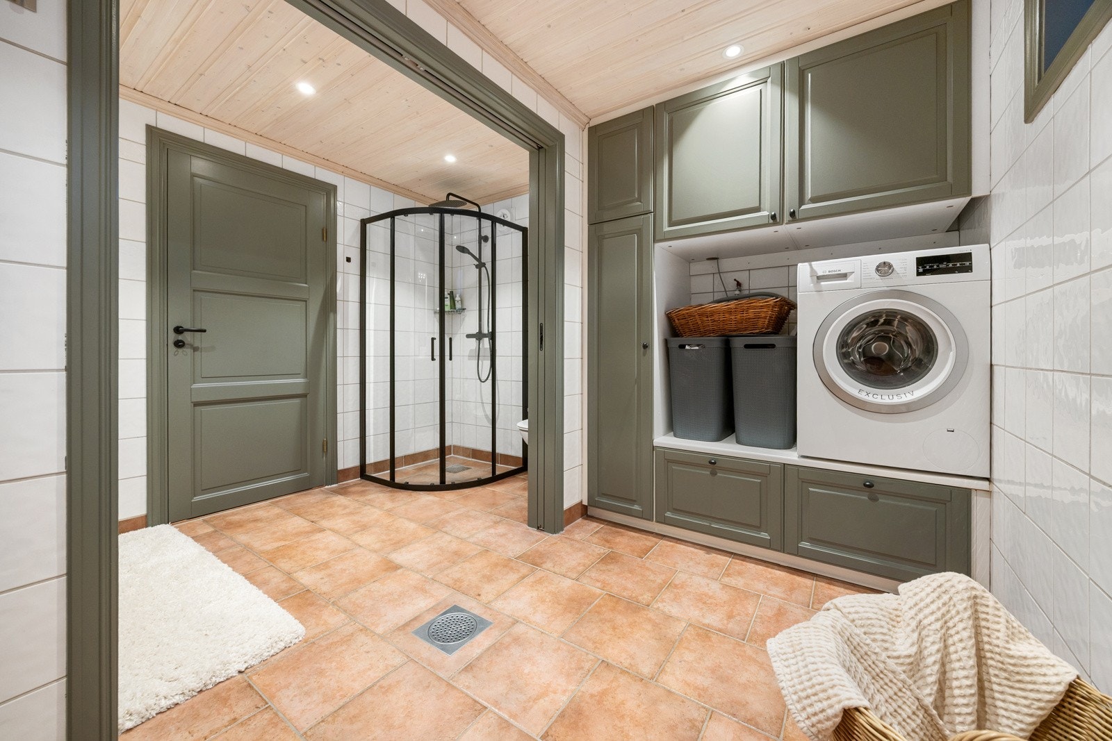 Romslig bad/vaskerom med flislagte vegger og flislagt gulv med elektriske varmekabler. Gulvet har to sluk, noe som gir god funksjonalitet både for baderomsbruk og klesvask.