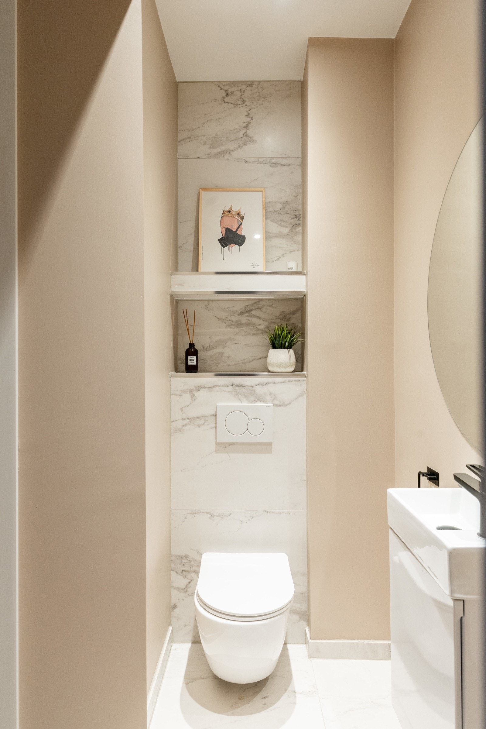 Toalettrom med flis på gulv og slette, malte vegg- og takflater. Rommet er innredet med veggmontert toalett og porselenservant med innredning. Galleribilde