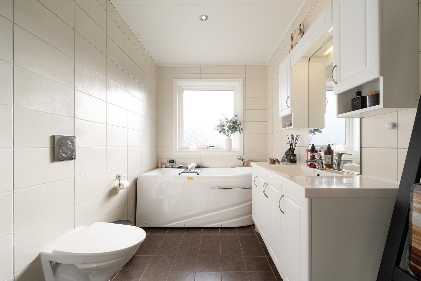 Flislagte bad utstyrt med vegghengt wc, badekar og innholdsrik, tidløs baderomsinnredning. Galleribilde