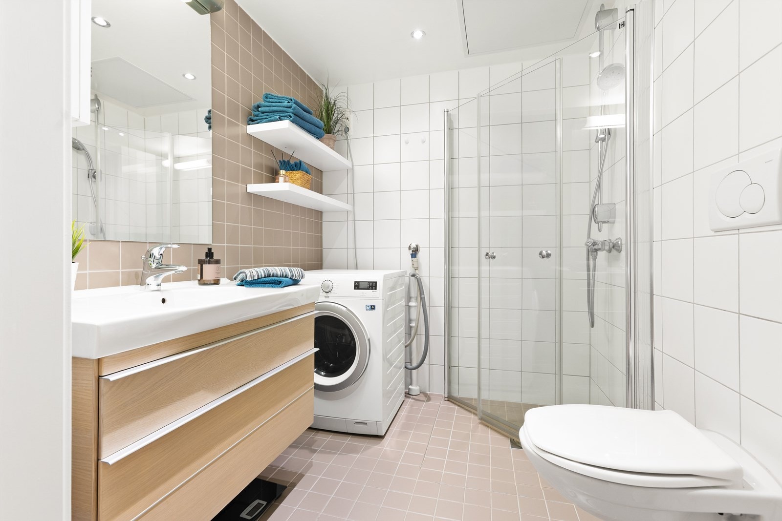 Pen bad utstyrt med heldekkende servant på møblement, speil med belysning og veggskap for ekstra oppbevaring. Videre har badet veggmontert toalett, dusjhjørne med innfellbare glassdører, samt opplegg for vaskemaskin og tørketrommel. Galleribilde