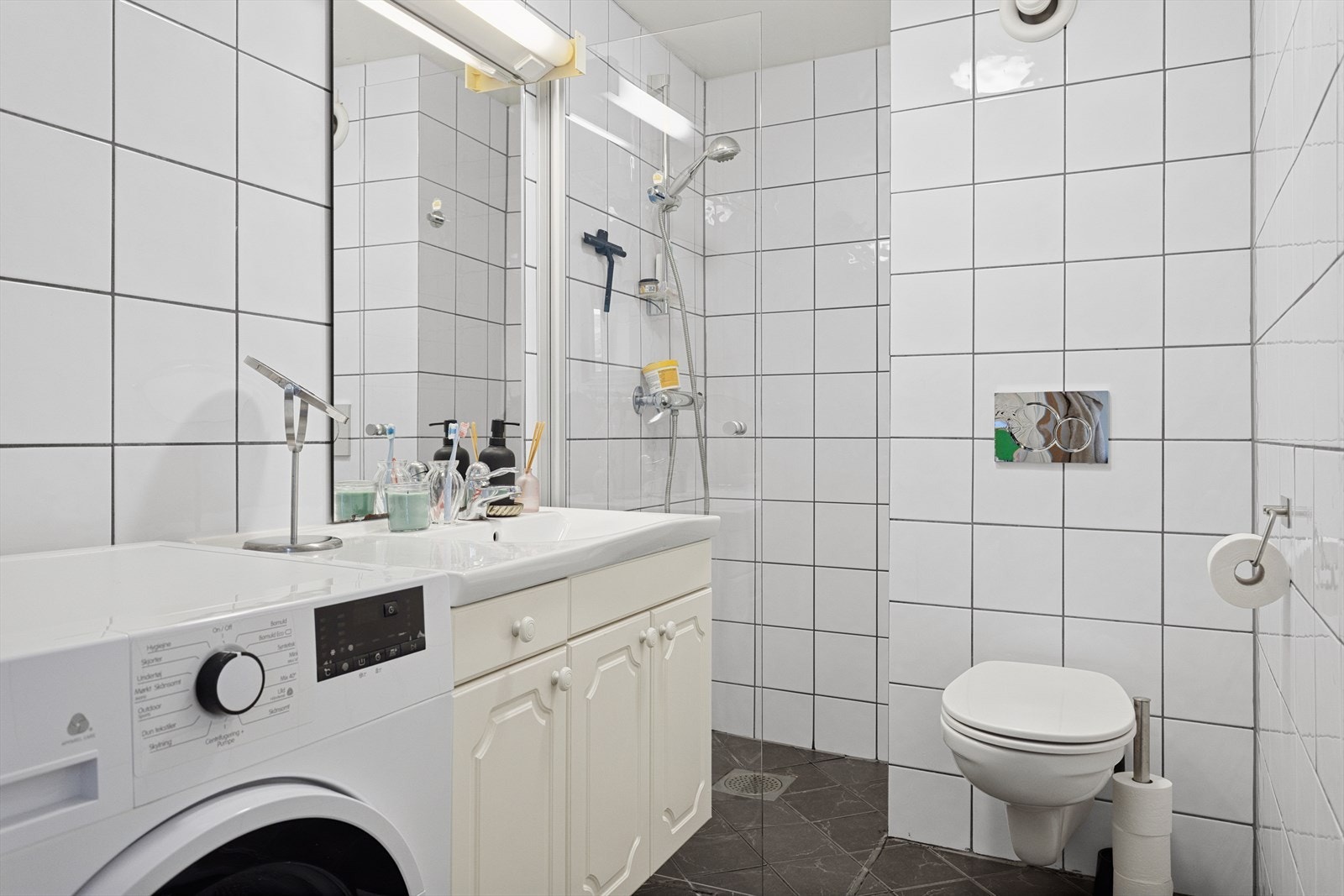 Baderommet har flis på gulv og flis på vegger. Malt overflate i himling. Gulvvarme. Utstyrt med servant, servantskap, mekanisk avtrekk, opplegg for vaskemaskin, veggmontert wc og innfellbare dusjdører. Galleribilde