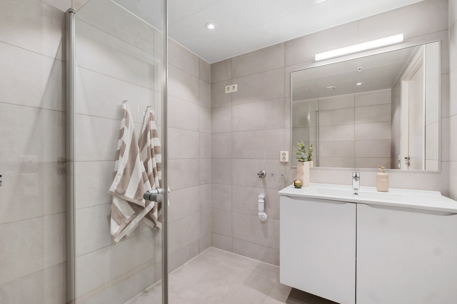 Badet er utstyrt med innredning med tilhørende speil, toalett, dusj og opplegg for vaskemaskin Galleribilde