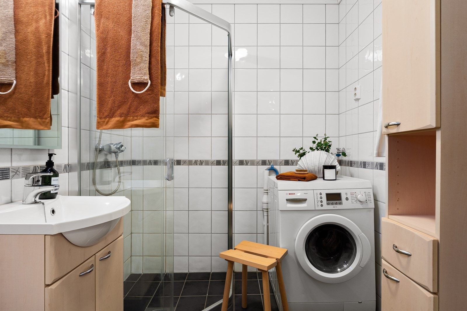 Badet er innredet med servant i møbel, skap, speil med lys, vegghengt toalett, dusj med skyvedør og opplegg for vaskemaskin. Galleribilde