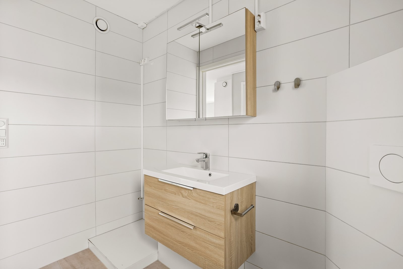 Badet er innredet med servantskap, speilskap, vegghengt toalett og en dusjnisje med glassvegg. Galleribilde