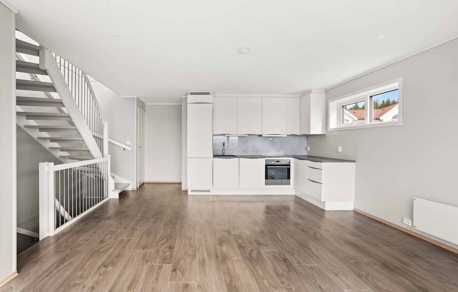 Kjøkkenet har en moderne innredning med hvite, glatte fronter, mørk benkeplate og en glassplate over benken. Galleribilde