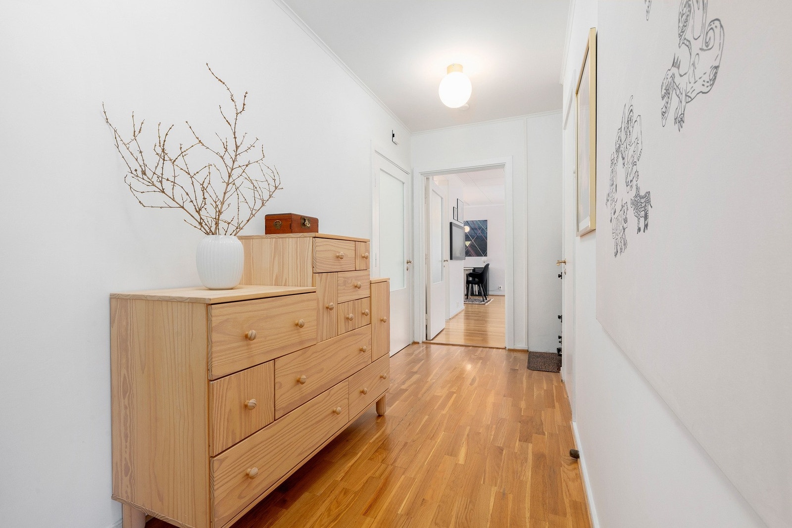 Romslig hall/ gang med lysmalte vegger og parkett på gulvet. Galleribilde