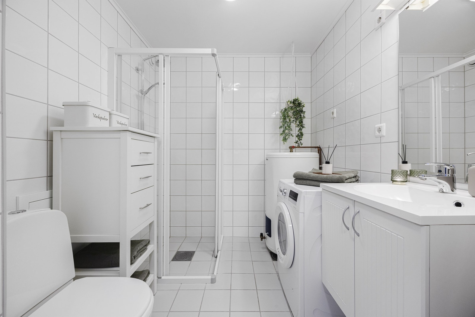 Tidløst bad med hvite fliser på vegger/gulv og hvite baderomsmøbler. Varmekabler. Galleribilde