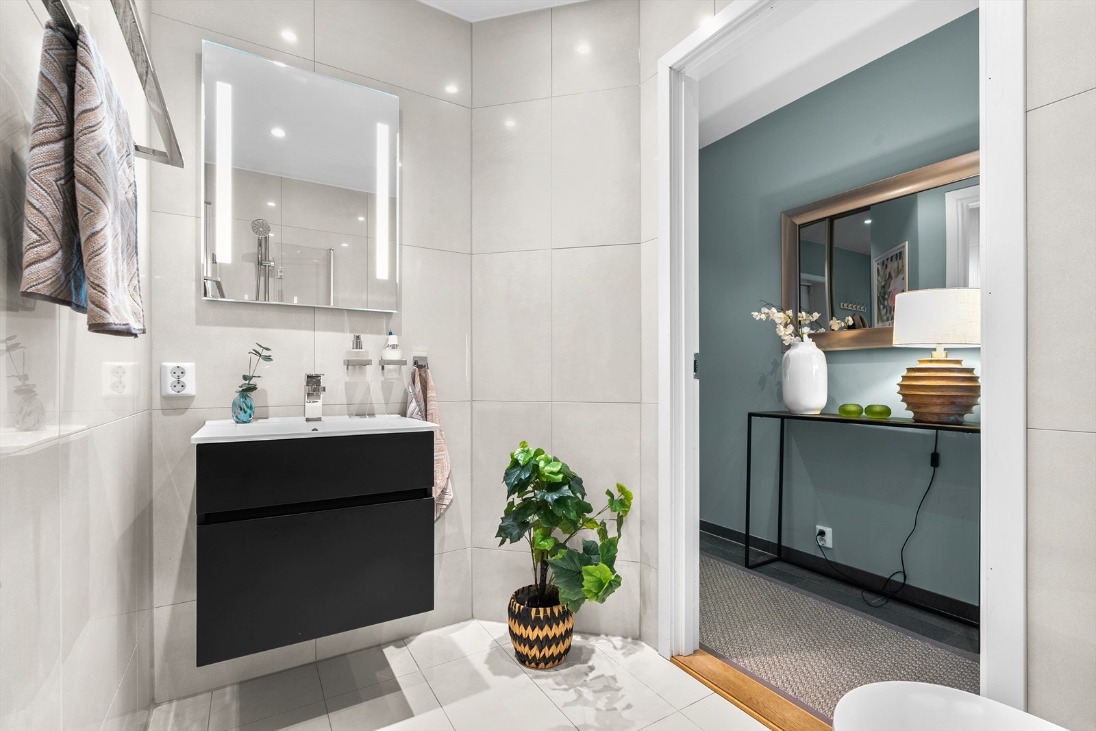 Her sett fra baderom ut mot entrè.
Badet er innredet med vegghengt klosett, servant med innredning, speil med lys og dusjhjørne med svingbare glassdører og har balansert ventilasjon. Galleribilde