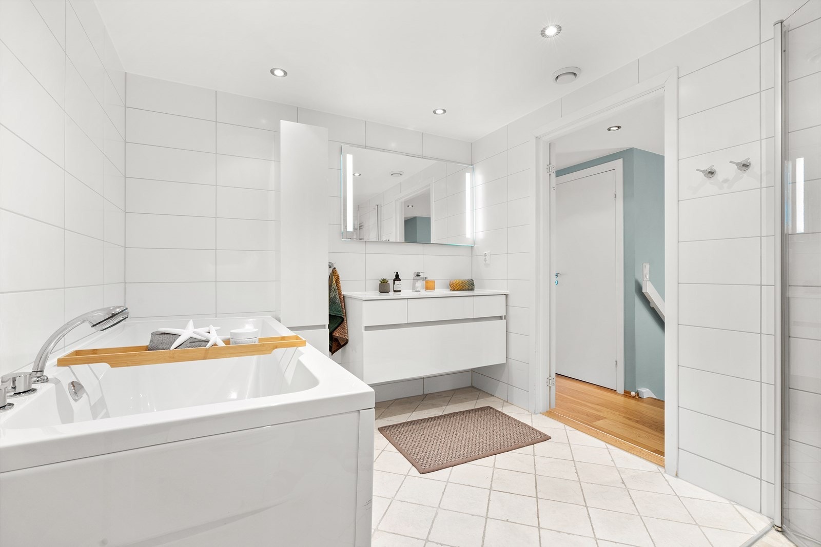 Videre er badet er innredet med vegghengt toalett, servant med tilhørende baderomsinnredning, speil med integrert belysning, samt både badekar og dusjhjørne med svingbare glassdører. Galleribilde