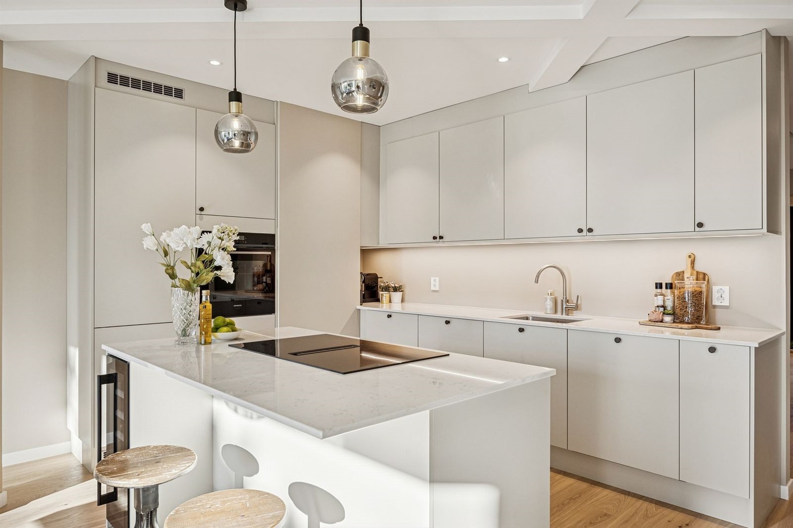 Kjøkkenet fra HTH har lyse fronter, kompositt benkeplater og en stor kjøkkenøy med integrert induksjonstopp og vinskap. Galleribilde