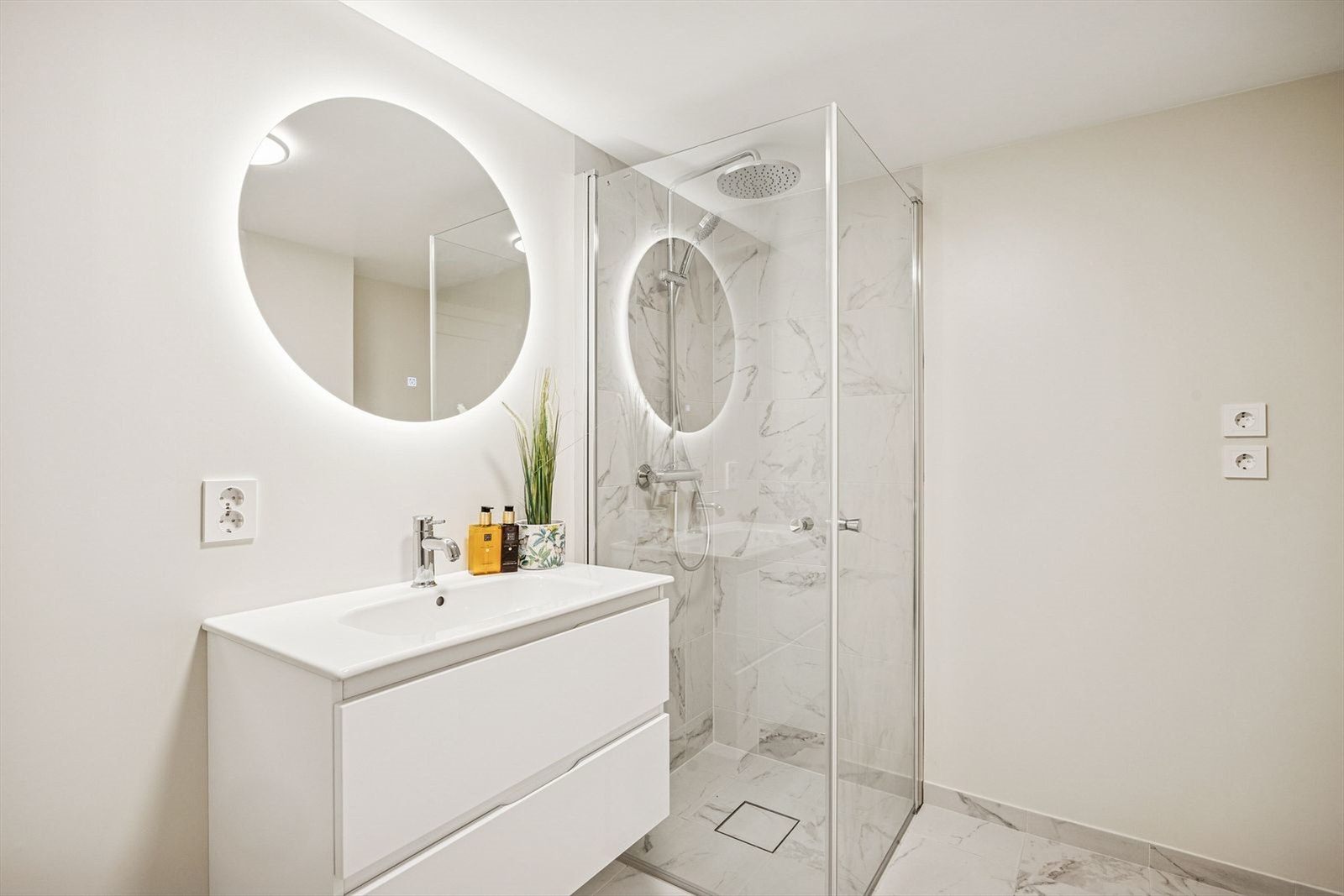 Badet i hybeldelen fremstår moderne og gjennomført med lyse fliser og stilrent interiør. Rommet er utstyrt med en romslig dusjnisje med glassvegger og regndusjhode. Varmekabler i gulvet sørger for god komfort året rundt. Galleribilde