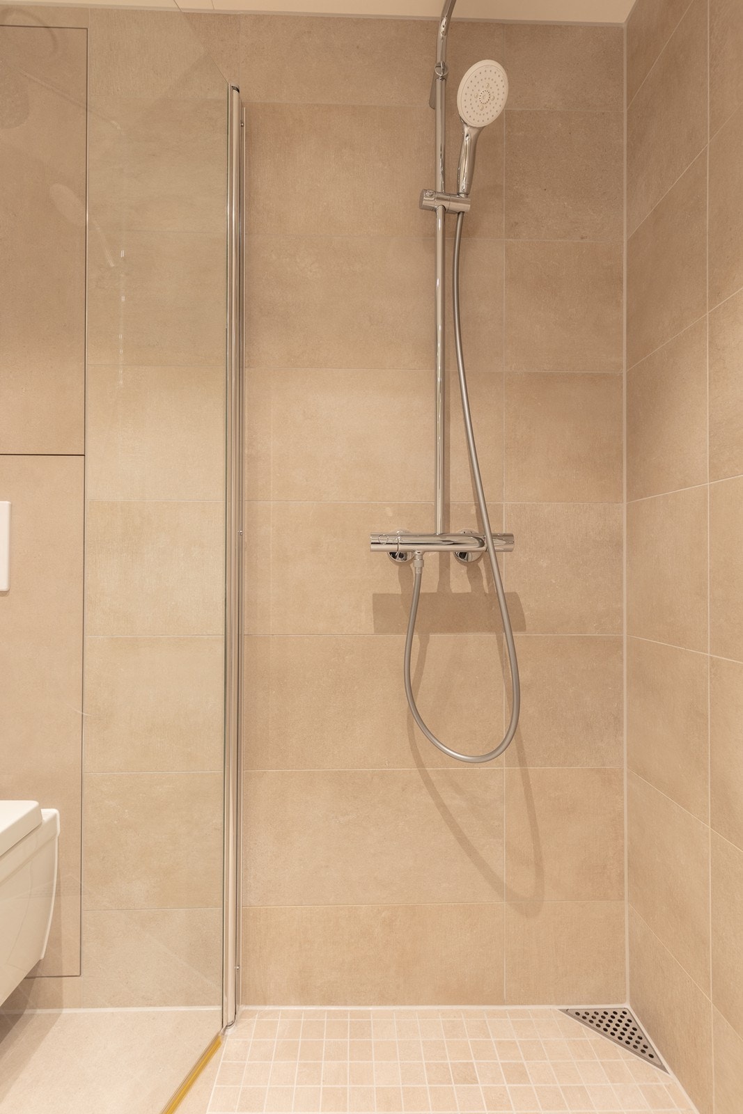 Dusjsonen har mosaikkfliser og et moderne hjørnesluk. Galleribilde