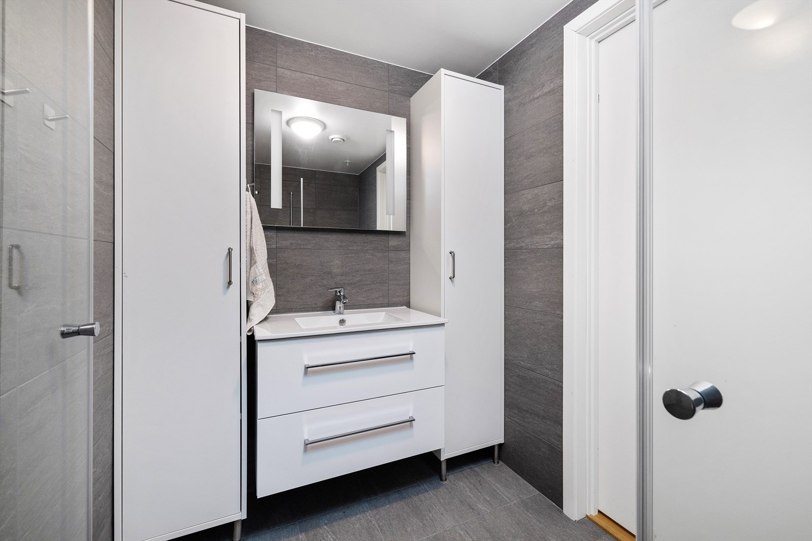 Baderomsinnredning med heldekkende servant og rikelig med oppbevaringsplass i skap. Galleribilde